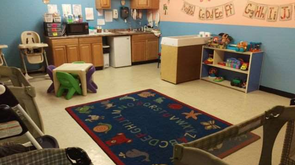 Infant/Toddler classroom with colorful rug, high chairs, and play area